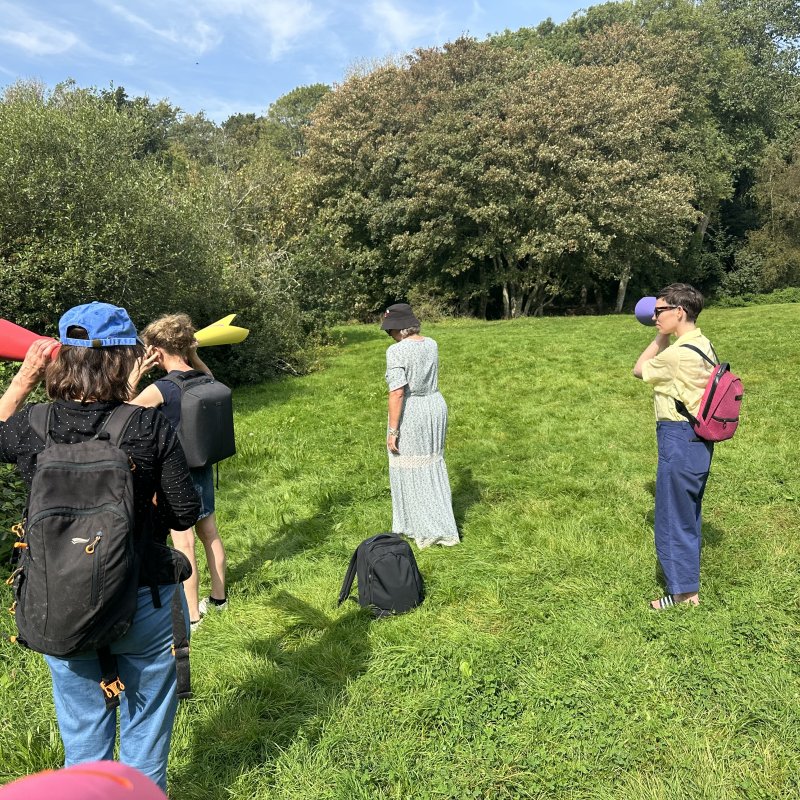 A group of people stood in a field using paper cones to listen to sounds